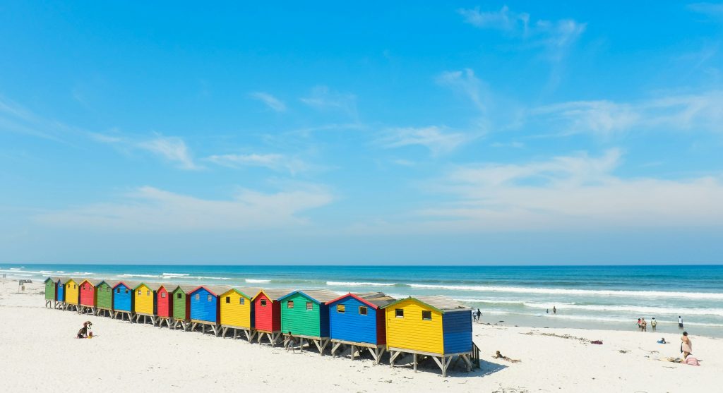Plage de Muizenberg à Cape Town avec ses cabines colorées et des surfeurs dans l’eau, idéale pour apprendre à surfer pendant un séjour linguistique.